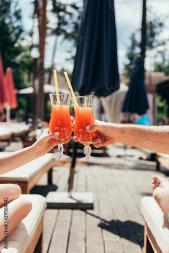 cropped view of boyfriend and girlfriend clinking glasses with refreshing drink