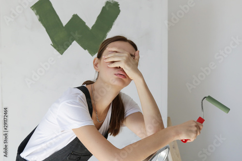 Fotografie Tired exhausted young woman having problem with painting wall in her apartment,