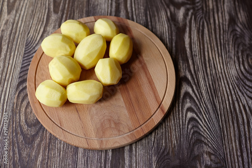 Potatoes on wooden chopping board on brown table. Cooking food from natural products. Root vegetable. Raw ingredient: uncooked whole peeled potatoes