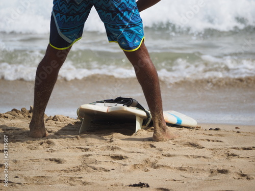 Crop image. A black surfer in shorts is getting ready to go into the ocean. Lifestyle.