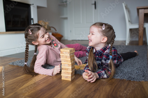 two laughing girls, best friends, play an educational game and stand a tower of cubes