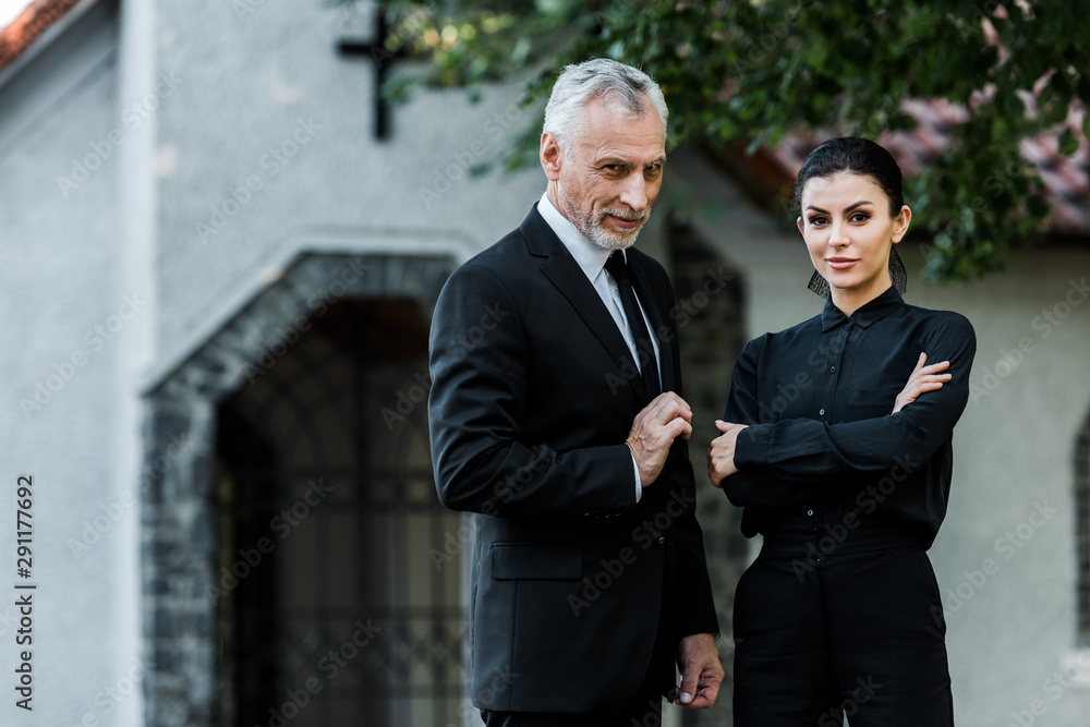 happy woman standing with crossed arms near bearded senior man in suit happy woman standing with crossed arms near bearded senior man in suit