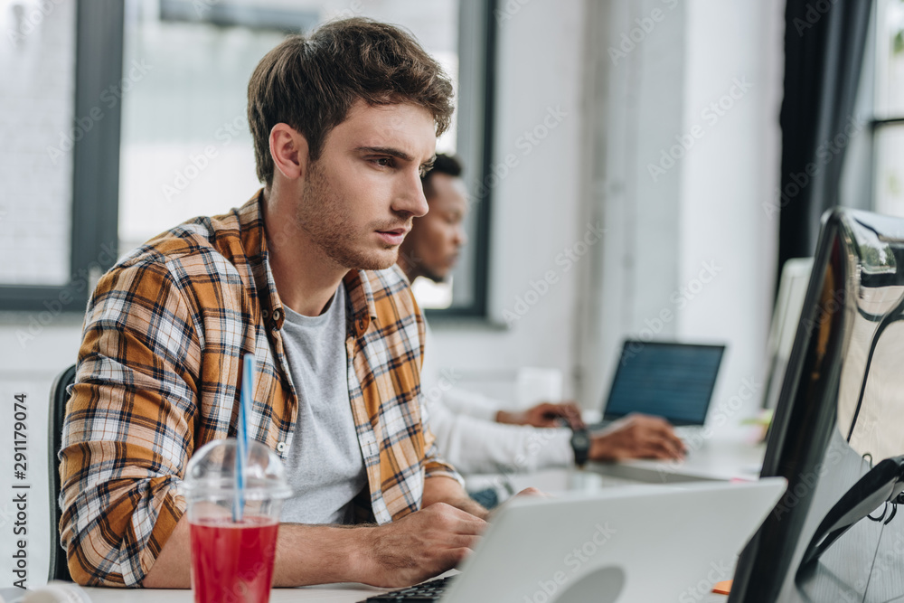 selective focus of attentive programmer working in office near african american colleague selective focus of attentive programmer working in office near african american colleague