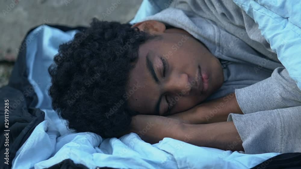 Homeless Afro-American teen boy sleeping on street, social insecurity concept Homeless Afro-American teen boy sleeping on street, social insecurity concept