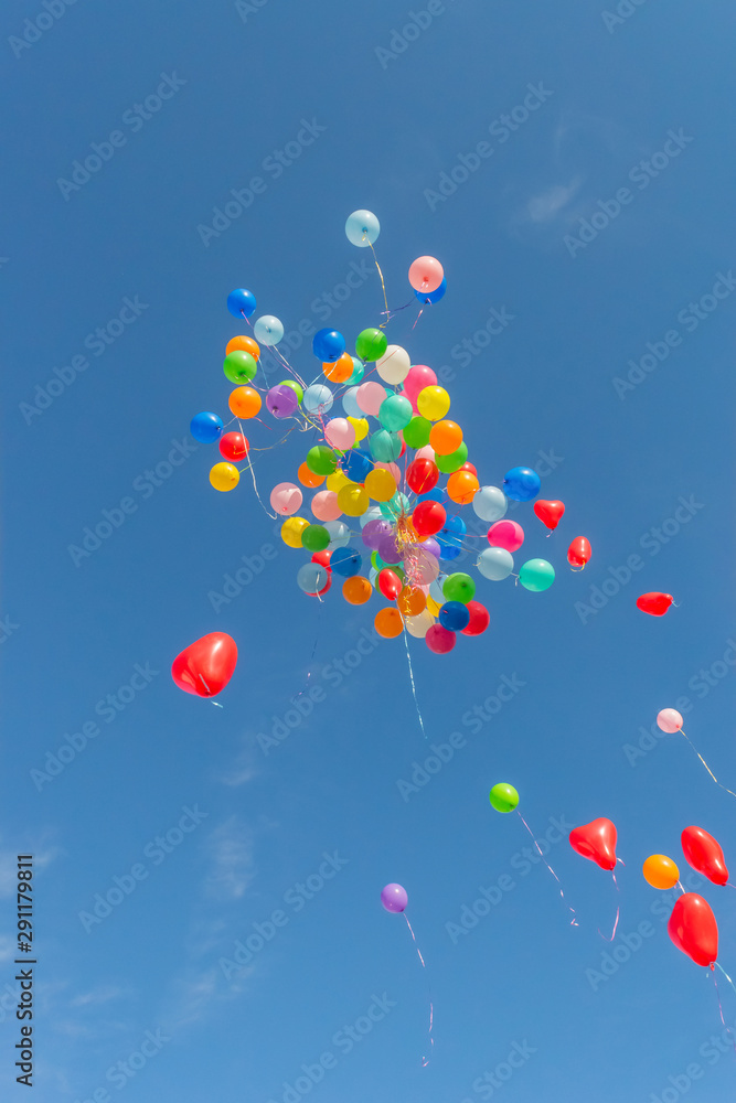 Large bunch of colorful party balloons floating up into the air against a sunny blue sky after a celebration, festival or carnival Large bunch of colorful party balloons floating up into the air against a sunny blue sky after a celebration, festival or carnival