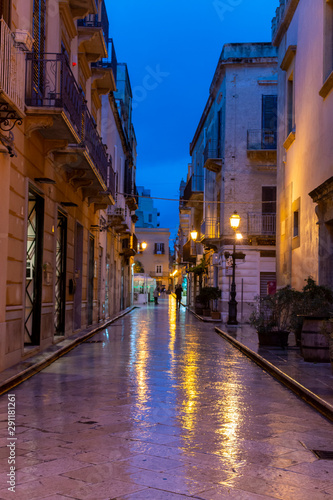 Old street in Marsala at night in rain with reflection of street lights on water  Sicily  Italy