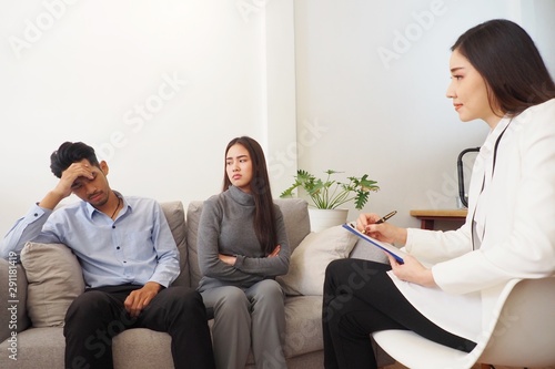 Professional Asian female psychiatrist giving advice to couple having serious relationship problem and difficulties in living together after marriage. Medical mental treatment provided by doctor