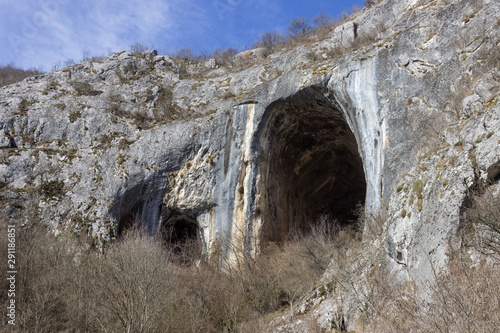 Huge, impressive entrance in to the cave Vladikine ploce on Old mountain, Serbia, blue sky and foreground bushes
