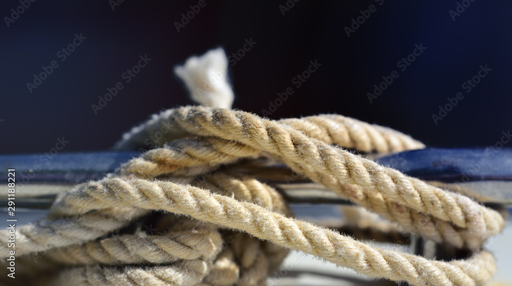 Closeup of an old twisted hemp rope attached to a boat with a knot in front of blue background