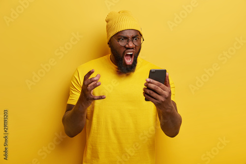 Canvas Print Annoyed black man with thick beard shouts angrily, has furious face expression,