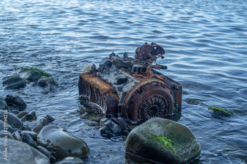 Old rusty engine lying among stones in the water.