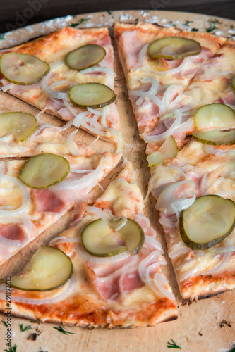 pizza with ham, pickles, onions on a wooden plate