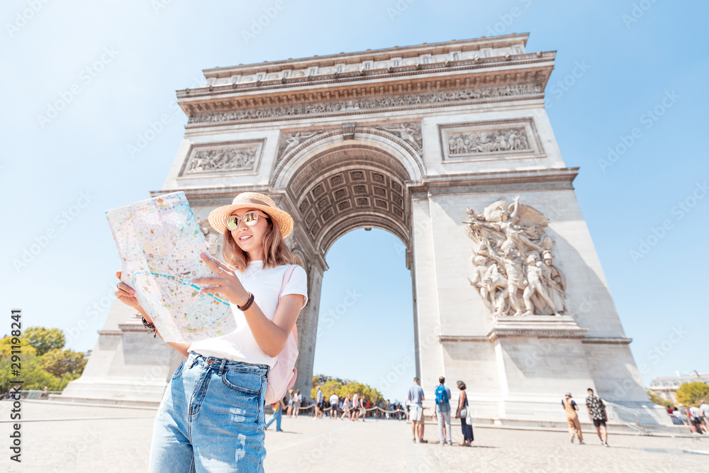 Happy Asian tourist girl enjoys the view of the majestic and famous Arc de Triomphe or Triumphal arch. Solo Travel and voyage to Paris and France - obrazy, fototapety, plakaty 
