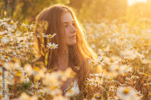 Side portrait of pretty blond woman sitting in chamomile field