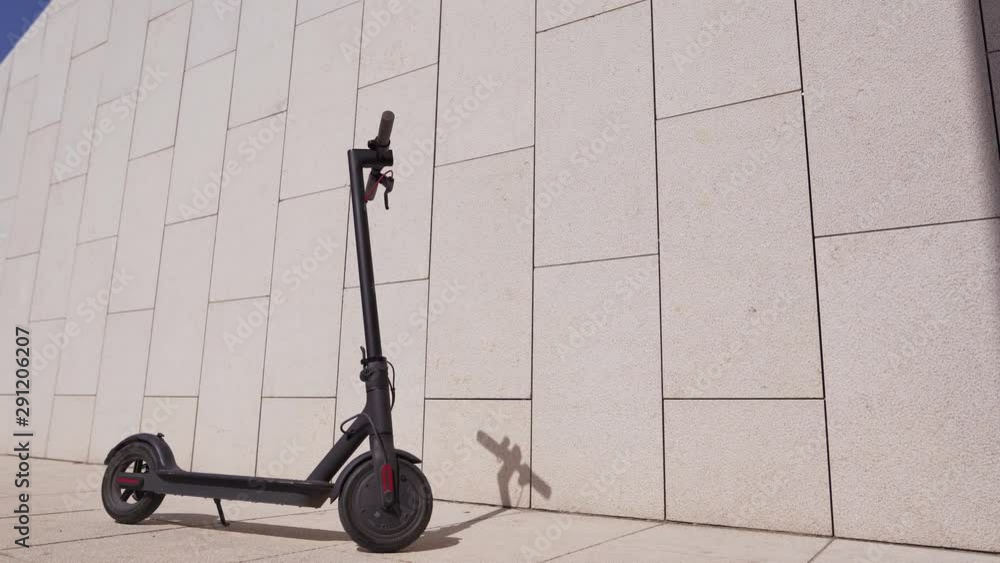 Black stylish electric scooter standing against a concrete wall on a sunny day. Environmentally friendly transport Black stylish electric scooter standing against a concrete wall on a sunny day. Environmentally friendly transport
