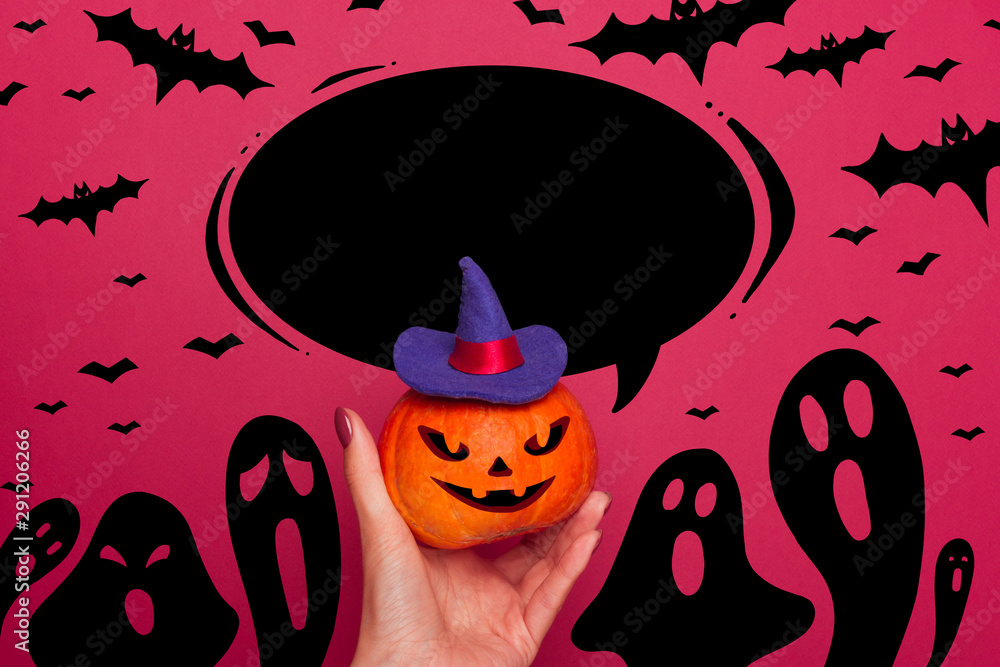 Happy halloween Pumpkin hold in a female hand in a blue witch hat with a white hand lettering in a black speech bubble. Black silhouettes of ghosts and bats.