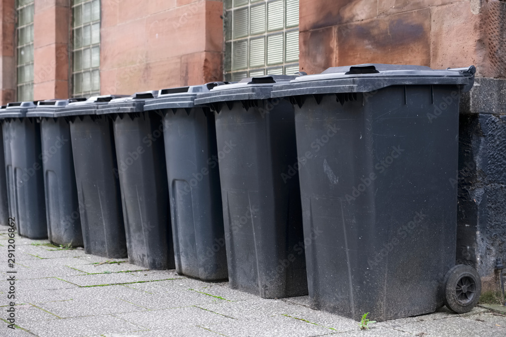 Black wheelie bins in a row on street with house numbers printed on front waiting for bin men to collect Black wheelie bins in a row on street with house numbers printed on front waiting for bin men to collect