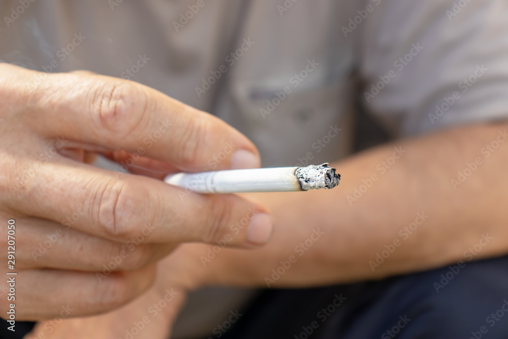Man holding a lighted cigarette in fingers with a lot of ashes, bad habbits and nicotine addiction concept Man holding a lighted cigarette in fingers with a lot of ashes, bad habbits and nicotine addiction concept
