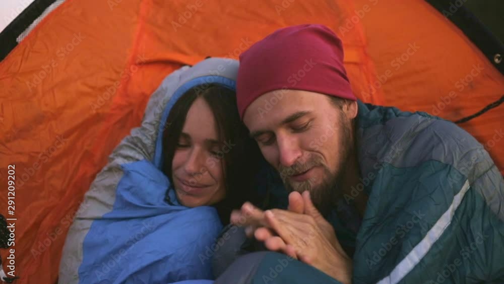 A man and a woman freeze in sleeping bags near a tent on a mountain hike. Slow motion shooting.