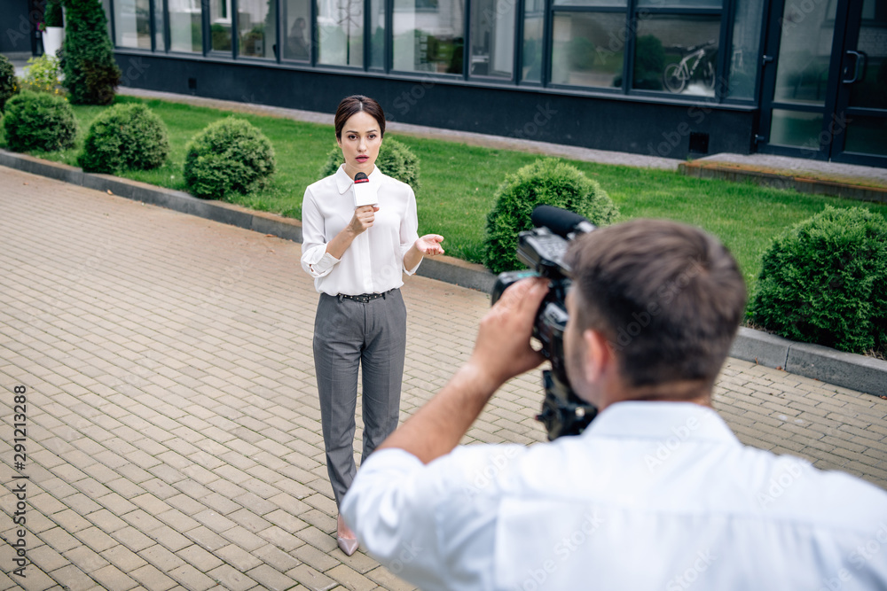 © LIGHTFIELD STUDIOS - selective focus of attractive journalist holding microphone and cameraman shooting her outside © LIGHTFIELD STUDIOS - selective focus of attractive journalist holding microphone and cameraman shooting her outside