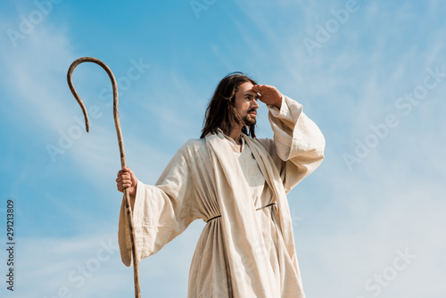 bearded man holding wooden cane against blue sky and clouds