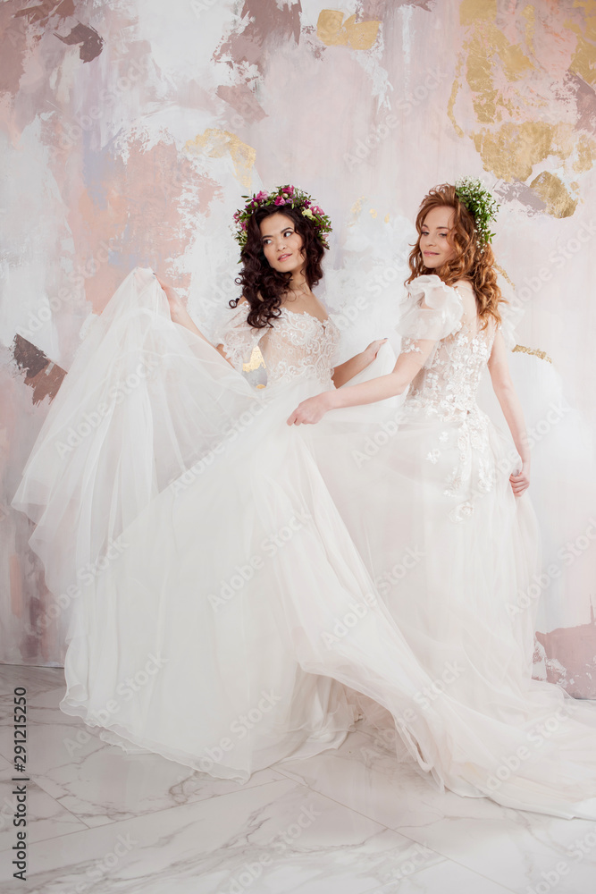 Two charming brides in beautiful spring wreaths on their heads. Beautiful young women in wedding dresses