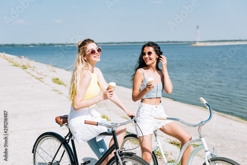 happy blonde and brunette girls riding bikes with ice cream near river in summer © LIGHTFIELD STUDIOS