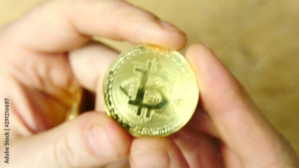 Mans hand picking up a gold btc bitcoin cryptocurrency coin, looking at it Mans hand picking up a gold btc bitcoin cryptocurrency coin, looking at it