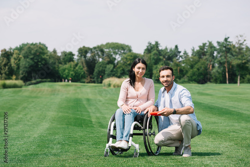 smiling man holding flying disc near young disabled girlfriend in park
