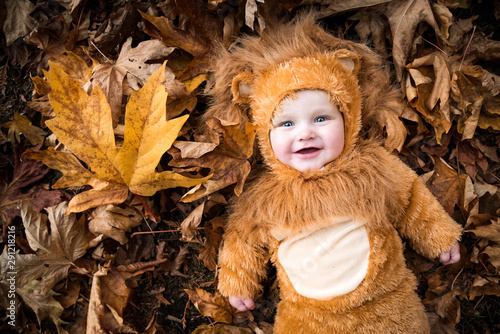 cute baby in Halloween costume laying in autumn leaves