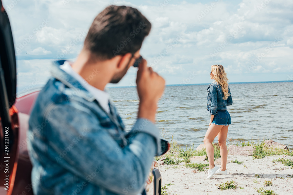 selective focus of blonde woman in denim shorts and jacket looking away