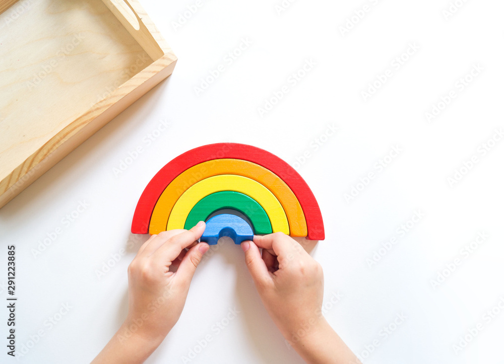Montessori wood rainbow material. A child plays with a toy with his hands. - obrazy, fototapety, plakaty 