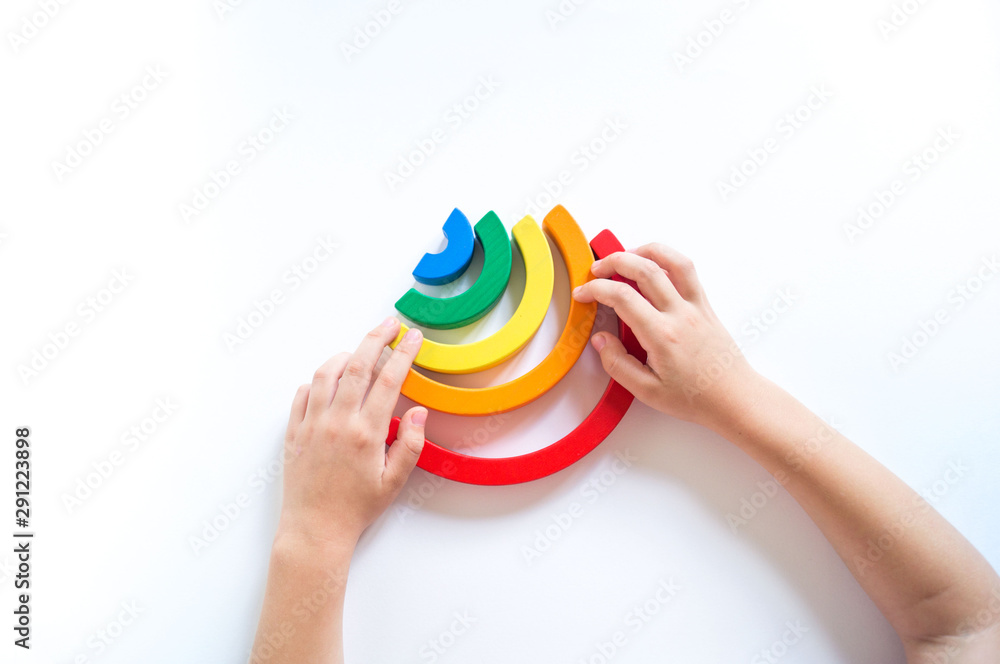 Montessori wood rainbow material. A child plays with a toy with his hands. Montessori wood rainbow material. A child plays with a toy with his hands.