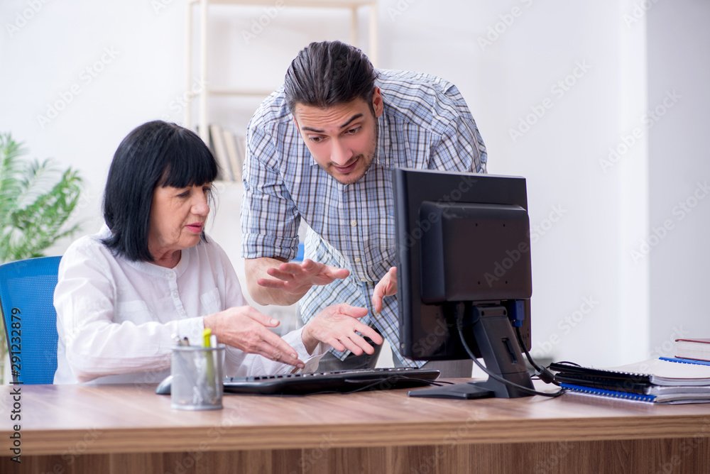 Young male employee explaining to old female colleague how to us Young male employee explaining to old female colleague how to us