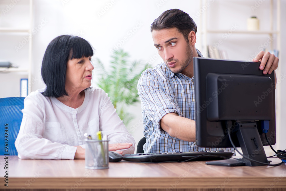 Young male employee explaining to old female colleague how to us Young male employee explaining to old female colleague how to us