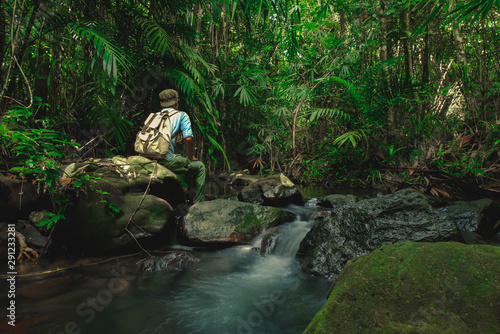 Man sitting on rock in rainforest with backpack among Small streams flow through abundant tropical forest concept summer vacations outside alone into the wild of Thailand,Phang Nga,Koh Yao Yai