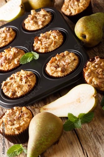 Freshly baked pear muffins with cinnamon and walnuts in a baking dish close-up. vertical