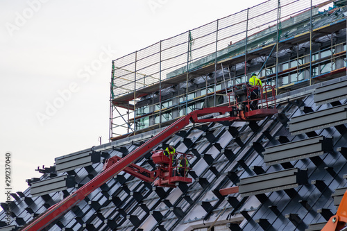 Baustelle mit Bauarbeitern auf roten Hebebühnen und roten Kränen begutachten die Fassade, die Glasfassade und das Gerüst der Architektur anhand der Baupläne photo