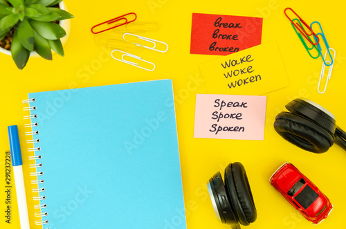 Foto Flat lay yellow desktop with blank spiral notepad, earphones, red car toy and sticky notes with handwritten irregular verbs