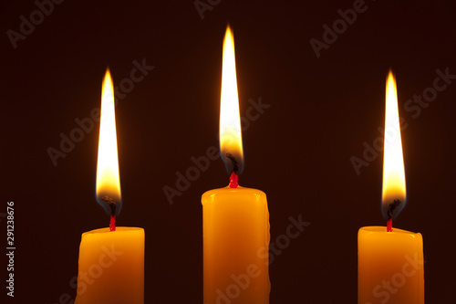 3 lighted candles on dark background. Horizontal shot.