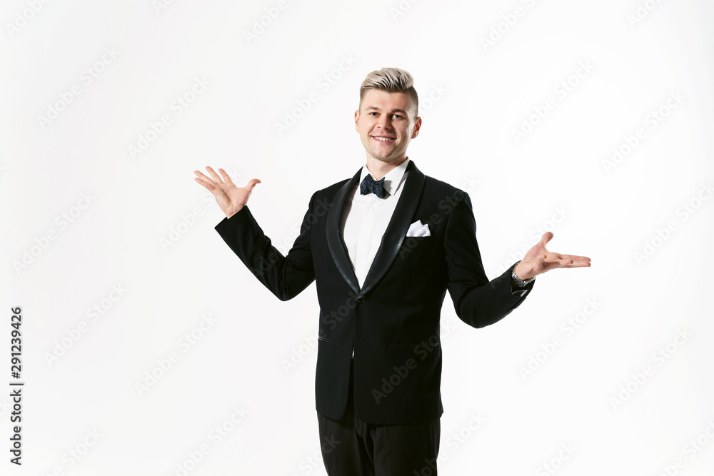 Portrait of young smiling handsome man in tuxedo stylish black suit, studio shot isolated on white background. Showman or toastmaster in jacket with bowtie Portrait of young smiling handsome man in tuxedo stylish black suit, studio shot isolated on white background. Showman or toastmaster in jacket with bowtie