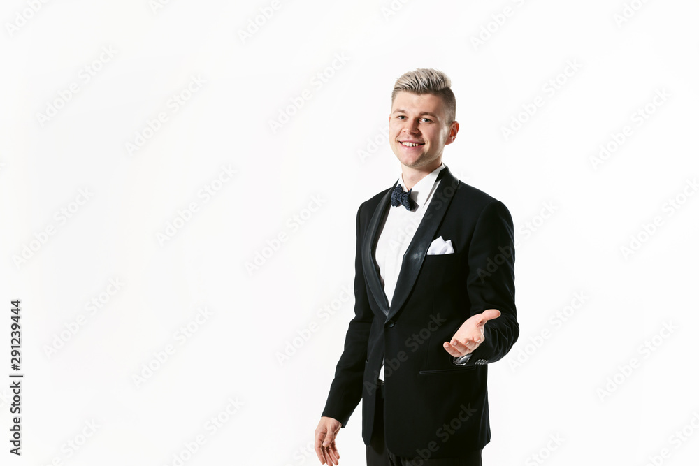 Portrait of young smiling handsome man in tuxedo stylish black suit, studio shot isolated on white background. Showman or toastmaster in jacket with bowtie Portrait of young smiling handsome man in tuxedo stylish black suit, studio shot isolated on white background. Showman or toastmaster in jacket with bowtie
