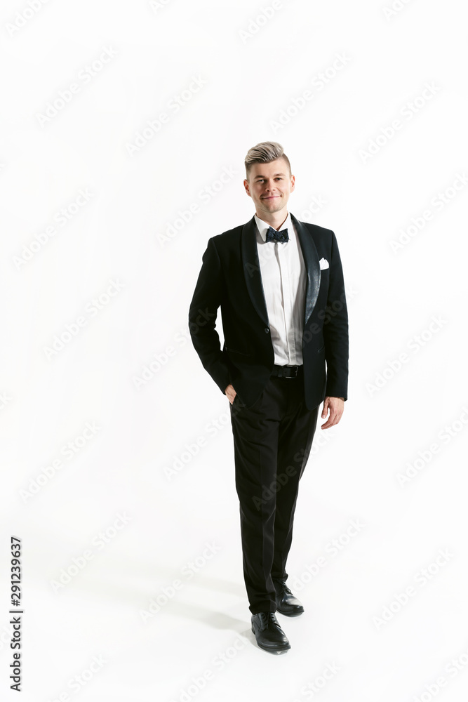 Portrait of young smiling handsome man in tuxedo stylish black suit, studio shot isolated on white background. Showman or toastmaster in jacket with bowtie Portrait of young smiling handsome man in tuxedo stylish black suit, studio shot isolated on white background. Showman or toastmaster in jacket with bowtie