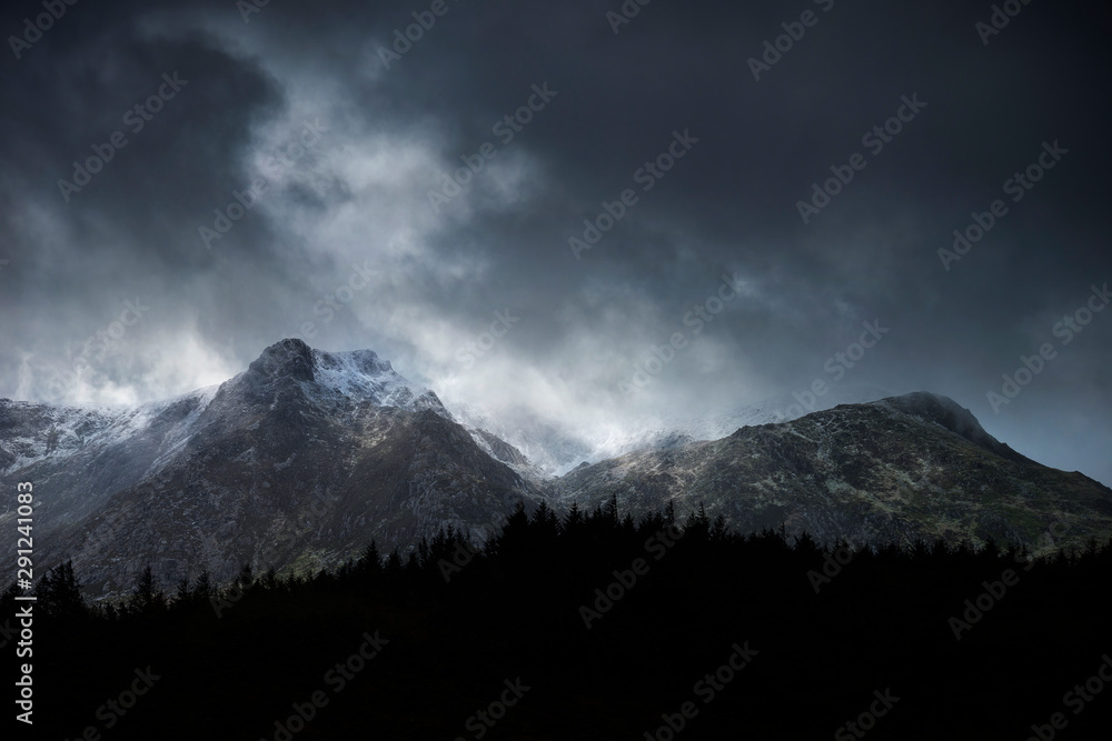 Stunning moody dramatic Winter landscape image of snowcapped Y Garn mountain in Snowdonia Stunning moody dramatic Winter landscape image of snowcapped Y Garn mountain in Snowdonia