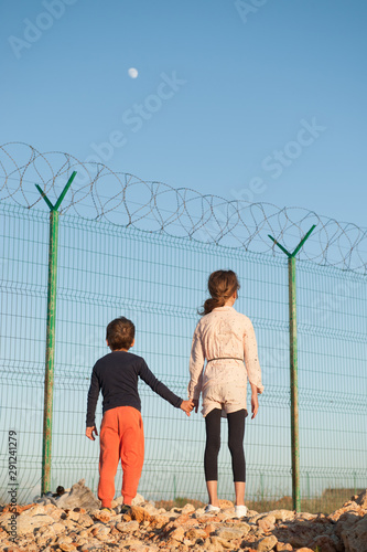 Valokuva poor refugees migrant kids on state border with high fence with barbed razor wir