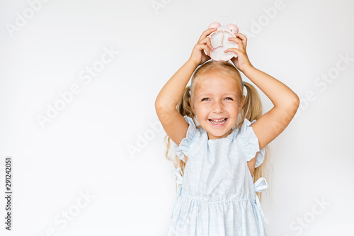 Adorable little girl holding alarm clock, copy space. Kid standing on white background. Time for school, promotion, sale. Excited girl at morning. People sincere emotions, childhood lifestyle