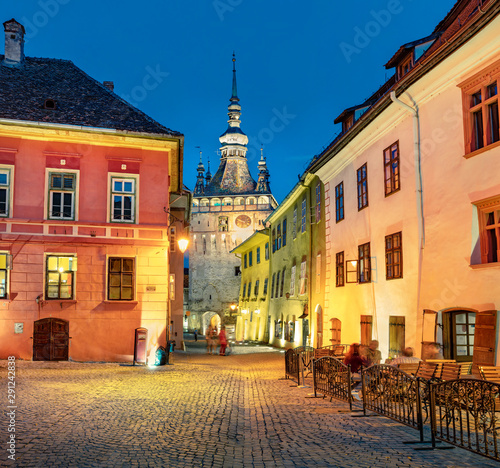 Picturesque evening view of famous medieval fortified city and the Clock Tower built by Saxons. Illuminated summer cityscape of Sighisoara, Transylvania, Romania, Europe. 