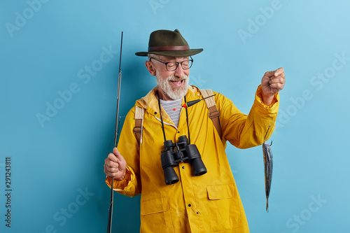 cheerful old man looking with pleased expression at fish, isolated blue background, stsudio shot. hobby, lifestyle