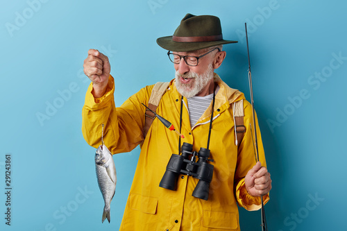 happy positive fishman looking at his fish, isolated blue background, good successful day for fishing. close up photo. photo