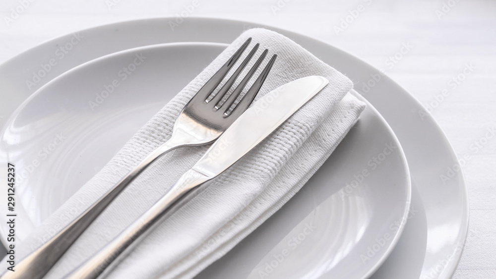 Close up of silverware fork and knife with napkin on white porcelaine plate. Copy space. Restaurant dinning concept. Close up of silverware fork and knife with napkin on white porcelaine plate. Copy space. Restaurant dinning concept.